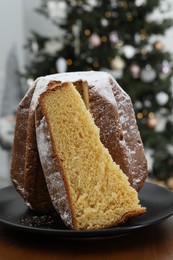 Photo of Delicious Pandoro cake decorated with powdered sugar near Christmas tree in room. Traditional Italian pastry