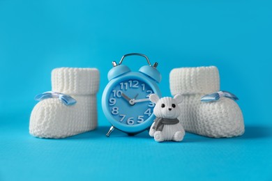 Photo of Alarm clock, toy bear and baby booties on light blue background. Time to give birth