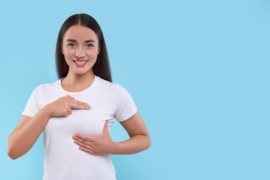 Beautiful happy woman doing breast self-examination on light blue background, space for text