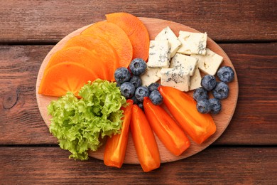 Delicious persimmon, blue cheese and blueberries on wooden table, flat lay