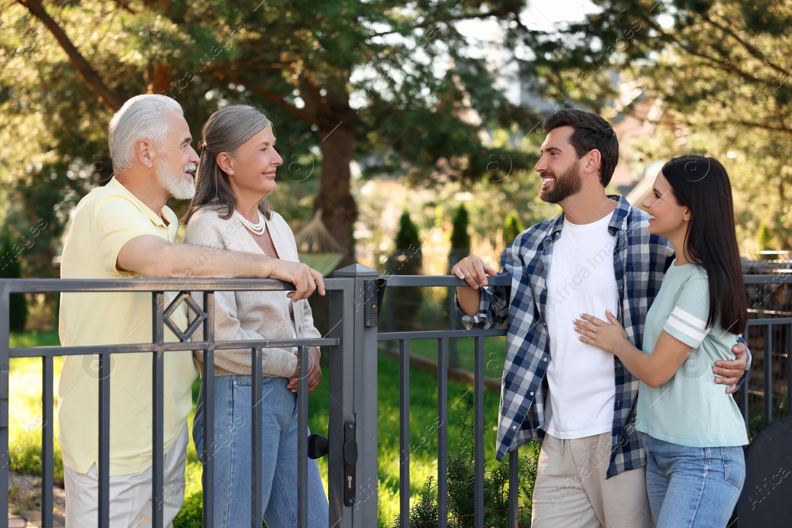 Photo of Friendly relationship with neighbours. Young family talking to elderly couple near fence outdoors