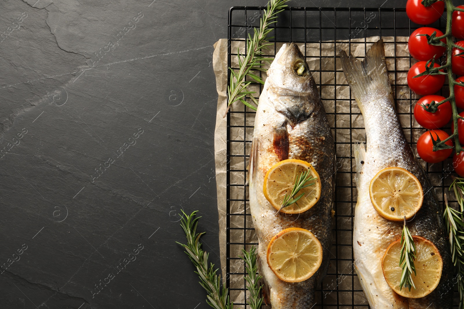 Photo of Baked fish with tomatoes, rosemary and lemon on black textured table, top view. Space for text