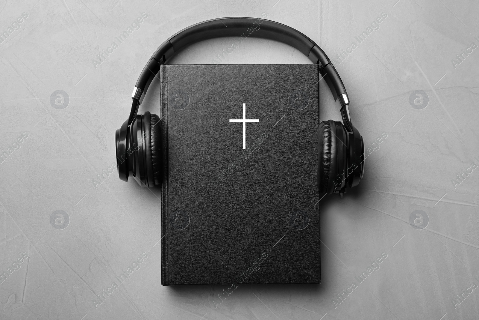 Photo of Bible and headphones on light grey background, top view. Religious audiobook