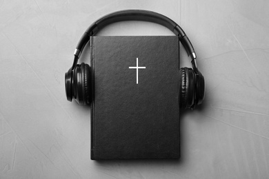 Photo of Bible and headphones on light grey background, top view. Religious audiobook