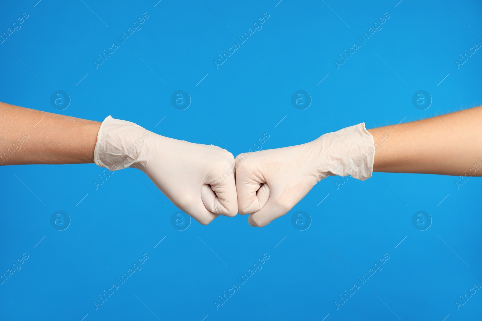Photo of Doctors in medical gloves making fist bump on light blue background, closeup