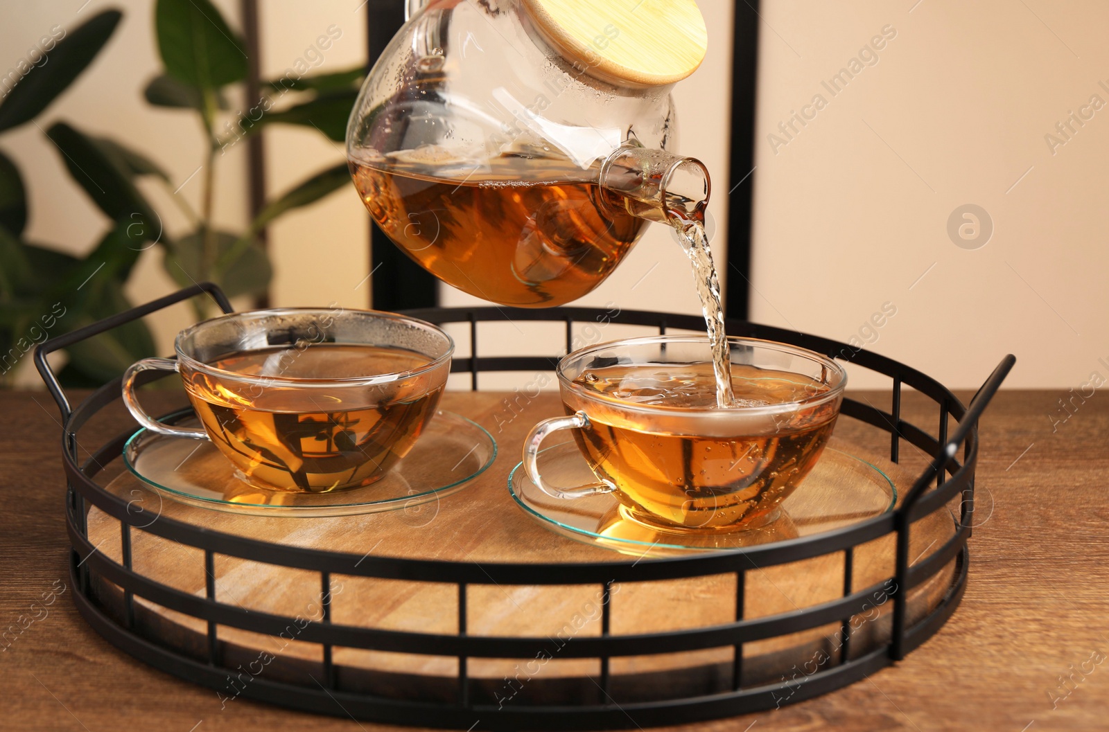 Photo of Pouring tasty tea into glass cup at wooden table, closeup