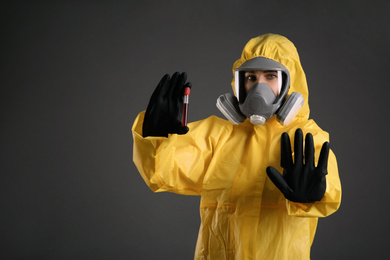 Photo of Woman in chemical protective suit holding test tube of blood sample on grey background. Virus research