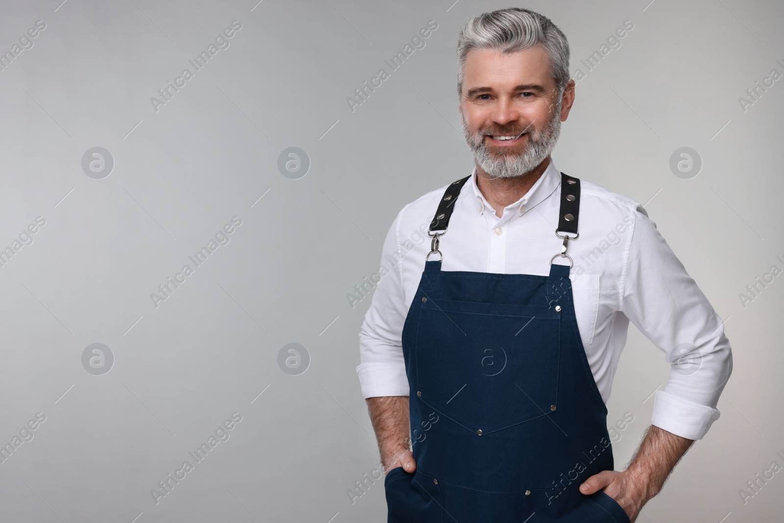 Photo of Happy man wearing kitchen apron on grey background. Mockup for design