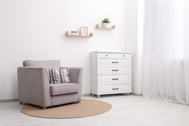 Stylish armchair and chest of drawers in room. Interior design