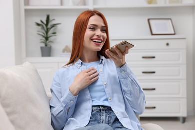 Photo of Happy woman sending voice message via smartphone on couch at home