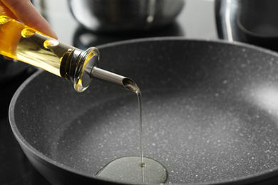 Photo of Woman pouring cooking oil from bottle into frying pan, closeup