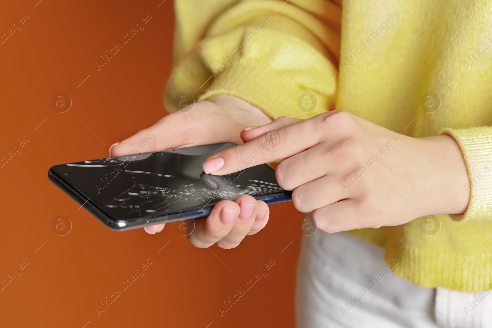 Photo of Woman holding damaged smartphone on orange background, closeup. Device repairing