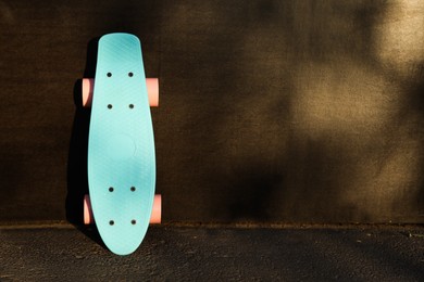 Photo of Modern light blue skateboard with pink wheels near black wall outdoors. Space for text