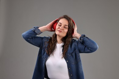 Portrait of beautiful young woman with headphones on grey background