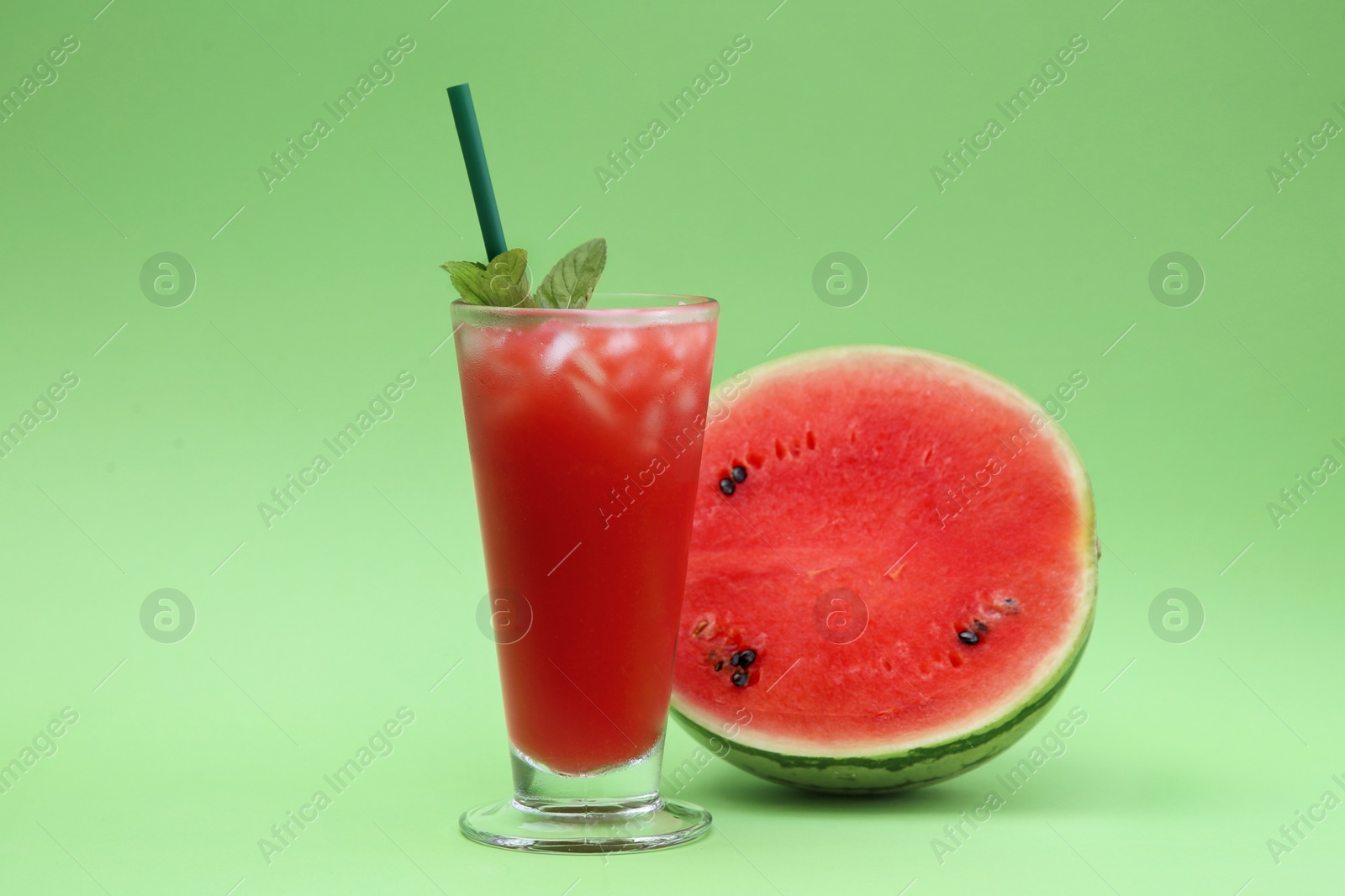 Photo of Glass of delicious drink with mint, ice cubes and cut fresh watermelon on light green background