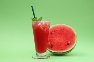 Glass of delicious drink with mint, ice cubes and cut fresh watermelon on light green background