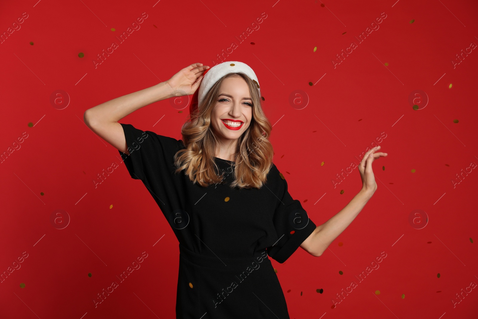 Photo of Happy young woman wearing Santa hat and confetti on red background. Christmas celebration