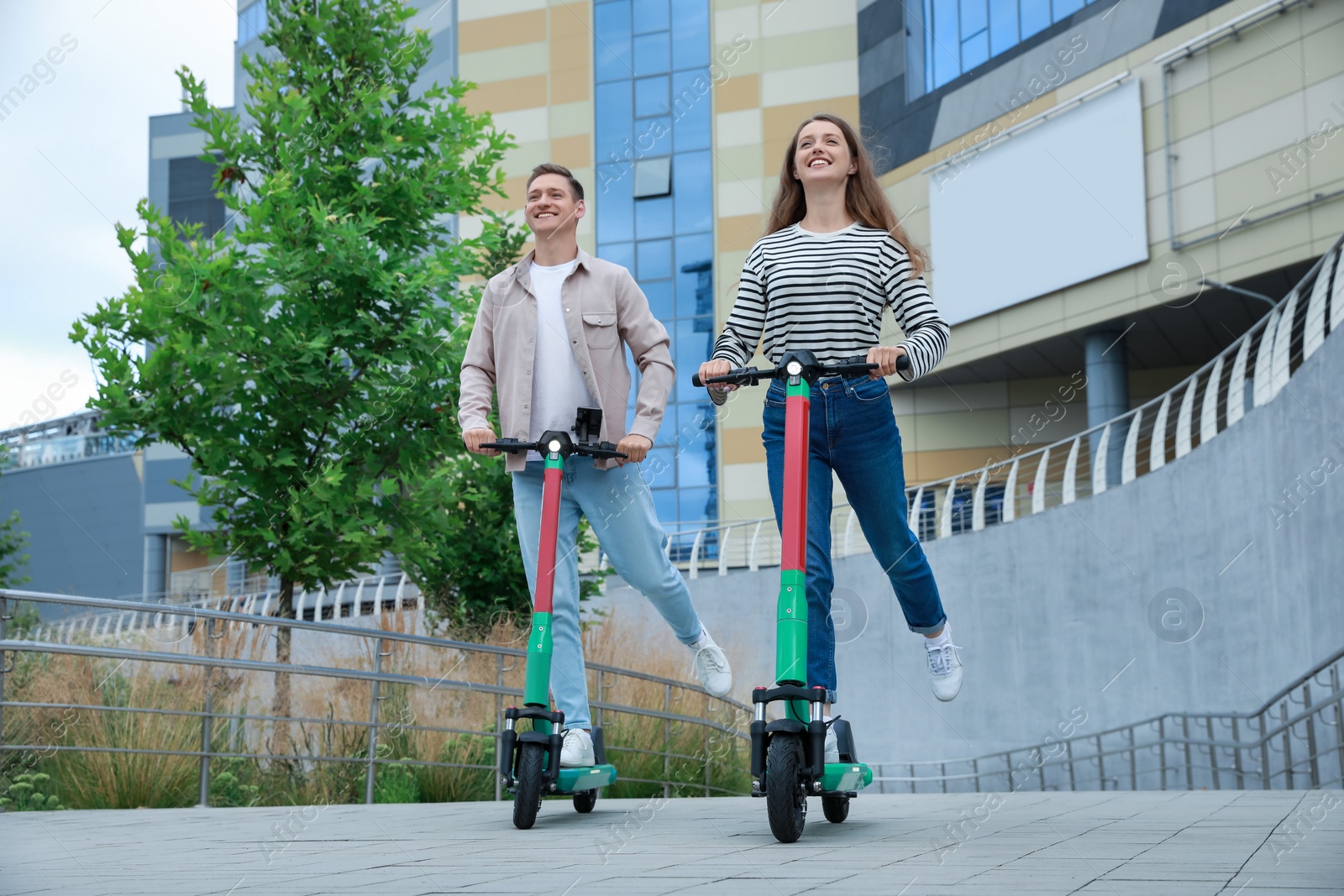 Photo of Happy couple riding modern electric kick scooters on city street