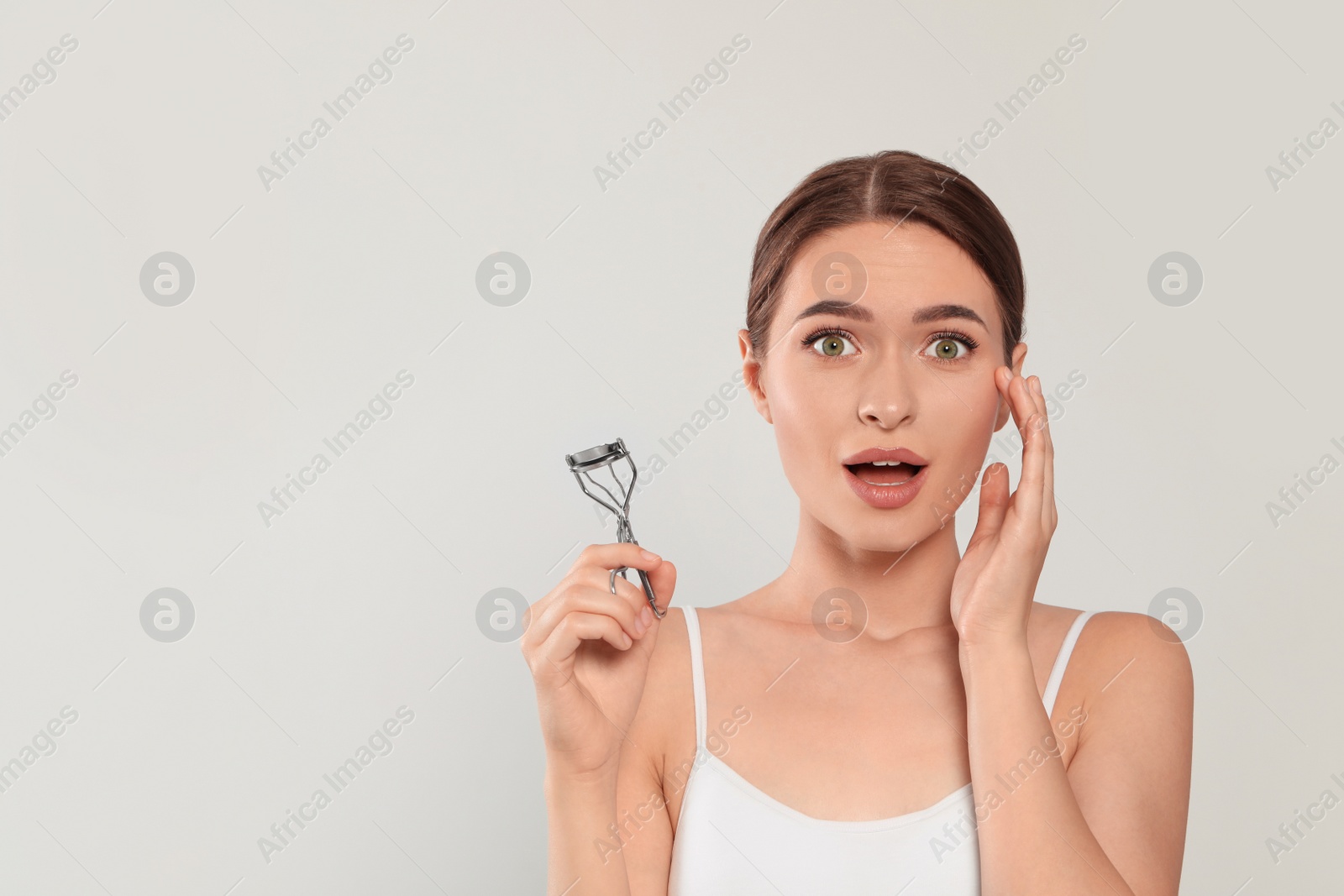 Photo of Emotional woman with eyelash curler on white background, space for text