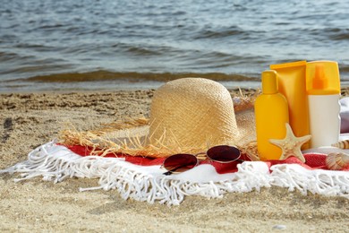 Sun protection products and beach accessories on blanket near sea, space for text
