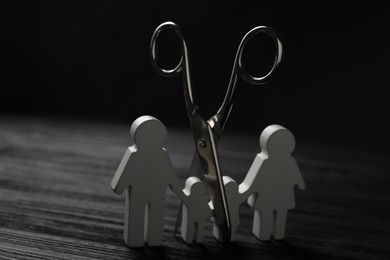 Photo of Family figure and scissors on black wooden table. Relationship problems concept