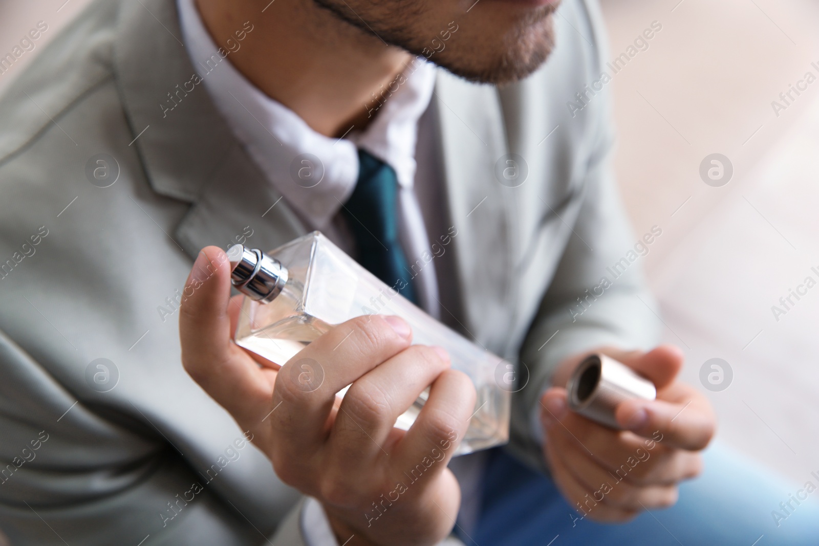 Photo of Businessman applying perfume on blurred background, closeup