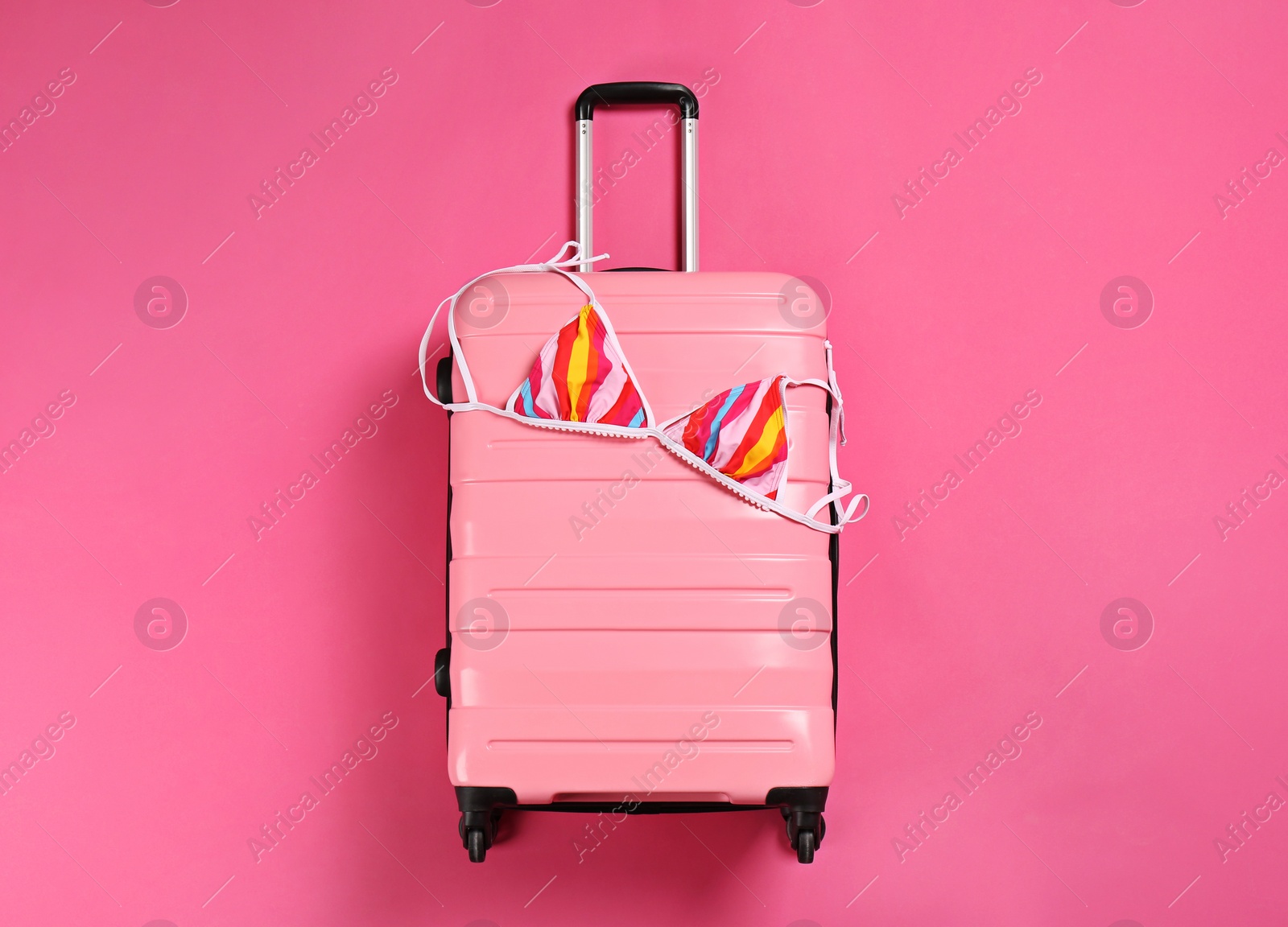 Photo of Stylish suitcase with bikini top on color background, top view