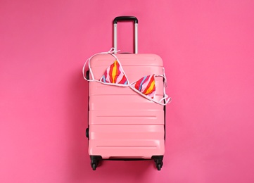 Photo of Stylish suitcase with bikini top on color background, top view
