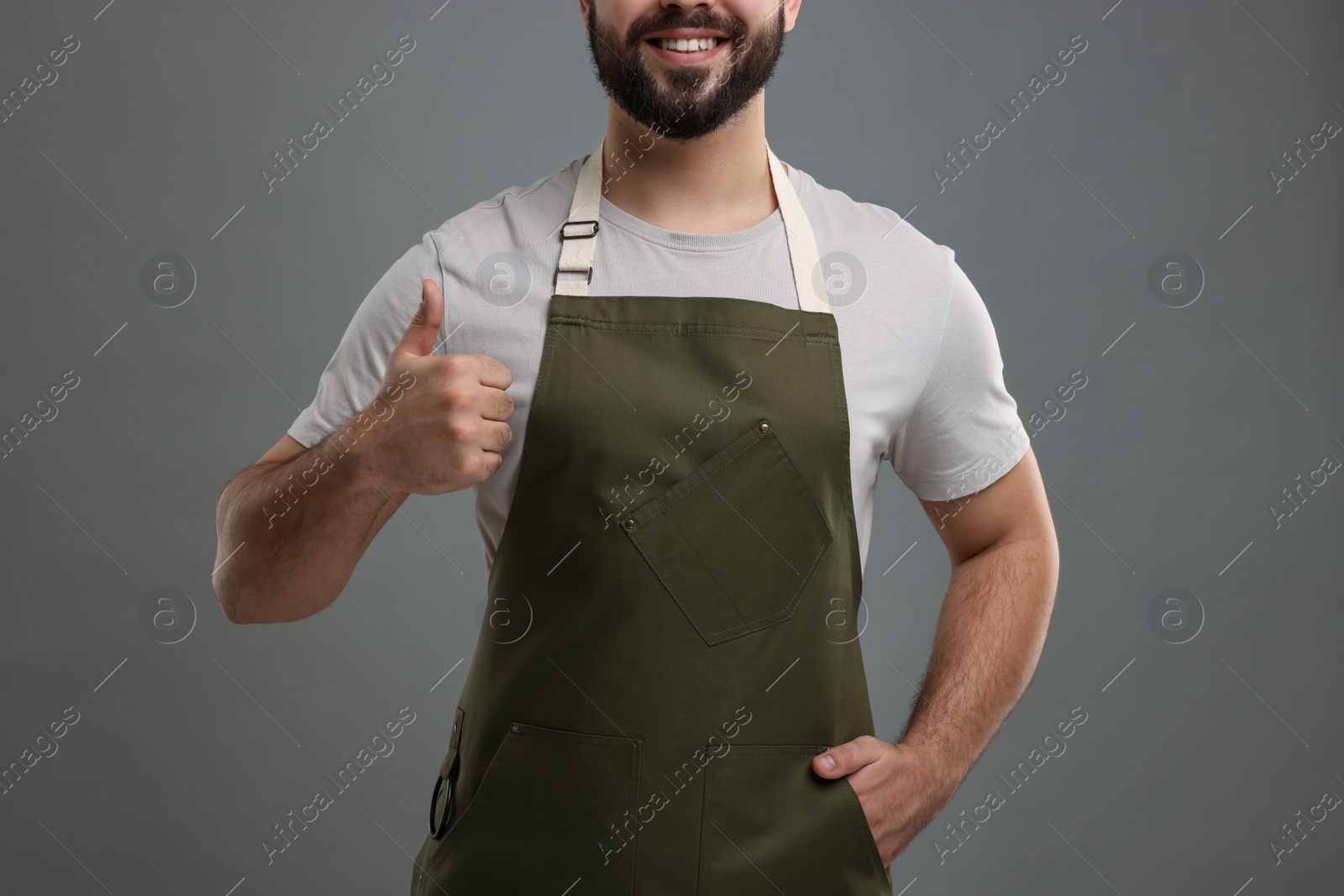 Photo of Smiling man in kitchen apron showing thumb up on grey background, closeup. Mockup for design