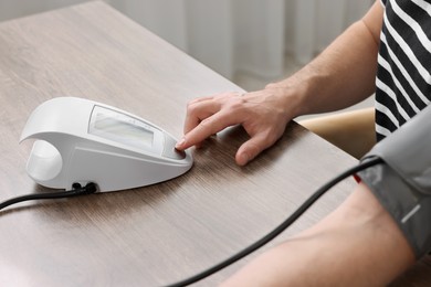 Photo of Man measuring blood pressure at wooden table, closeup