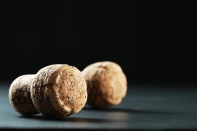Photo of Corks of wine bottles with grape images on black table, closeup. Space for text