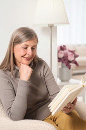 Photo of Beautiful senior woman reading book in armchair at home