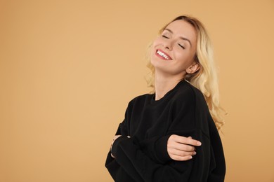 Happy woman in stylish warm sweater on beige background. Space for text