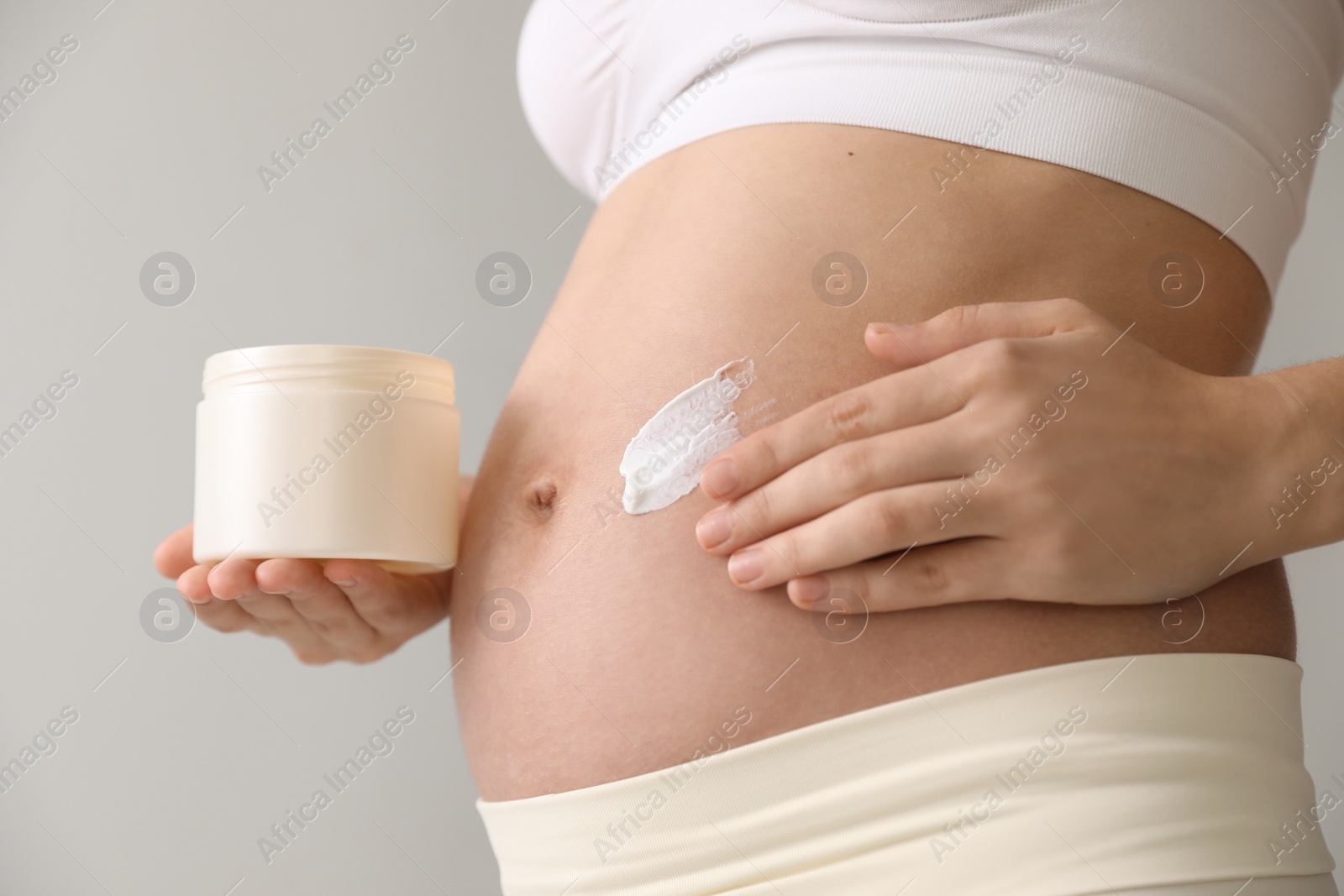 Photo of Young pregnant woman with cosmetic product on grey background, closeup