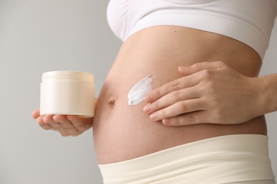 Photo of Young pregnant woman with cosmetic product on grey background, closeup
