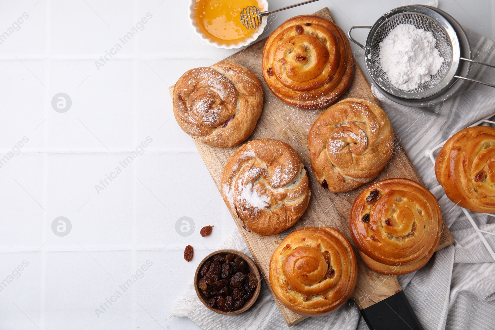 Photo of Sweet buns. Delicious rolls with raisins and powdered sugar on white tiled table, flat lay. Space for text