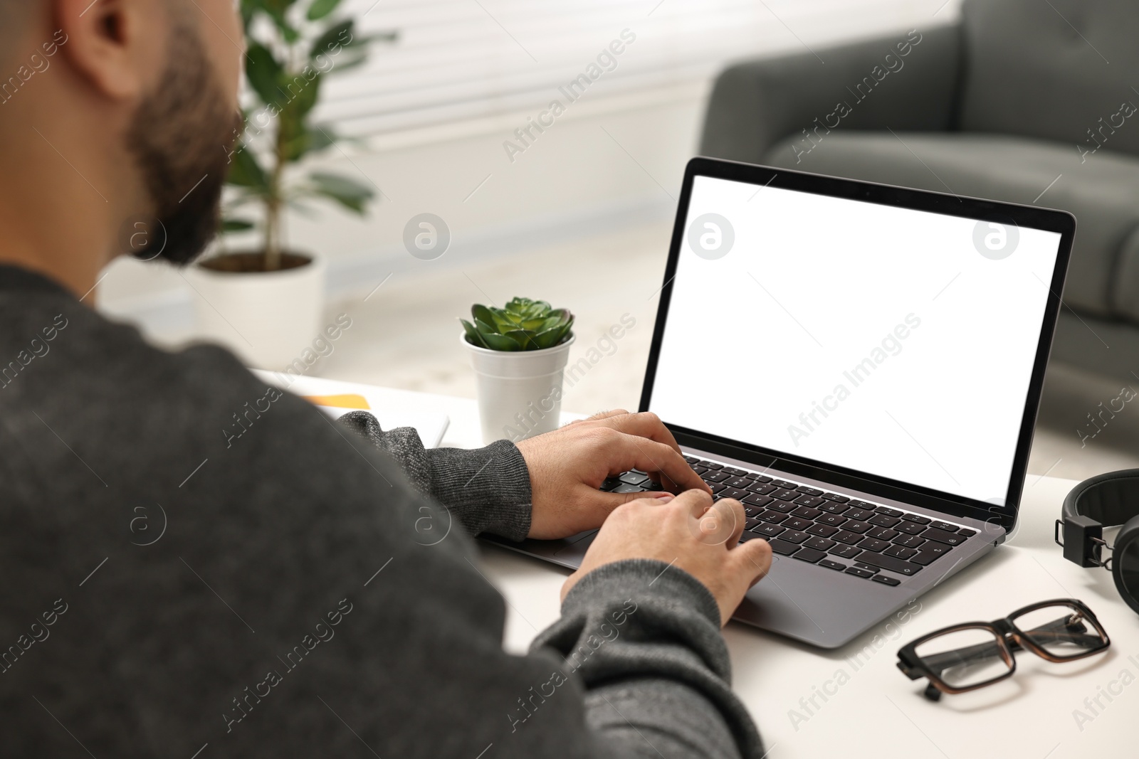 Photo of E-learning. Young man using laptop at white table indoors, closeup