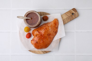 Photo of Fresh marinade and raw chicken fillets on white tiled table, top view