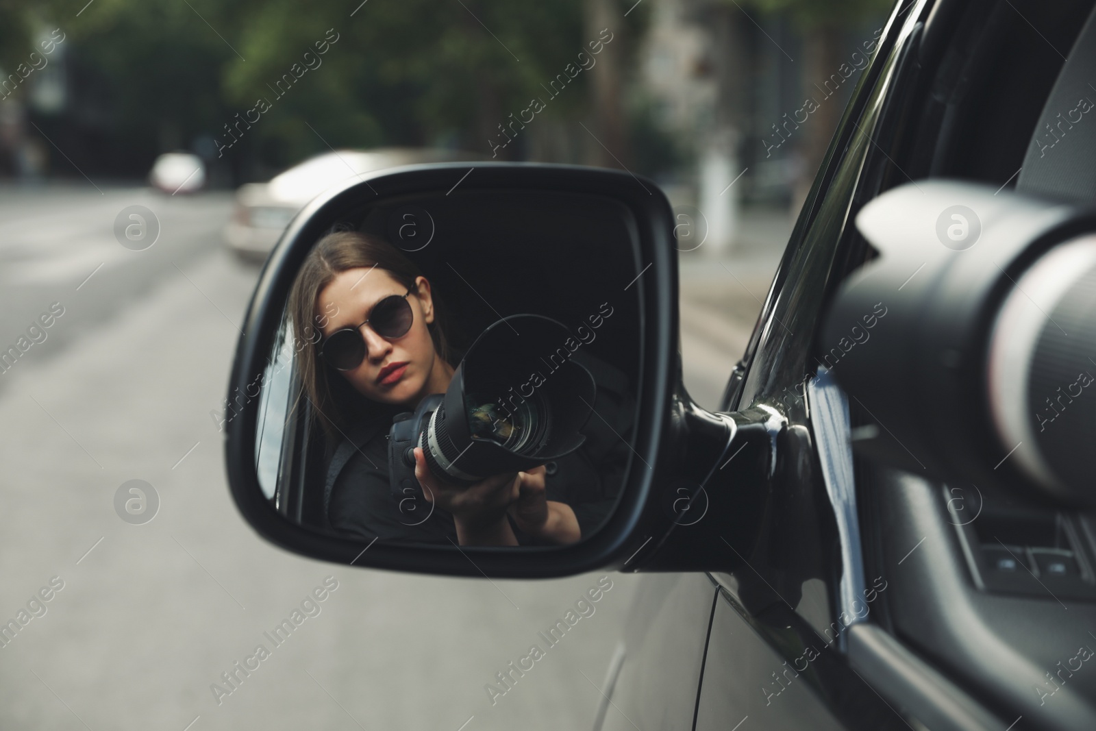 Photo of Private detective with camera spying from auto, view through car side mirror