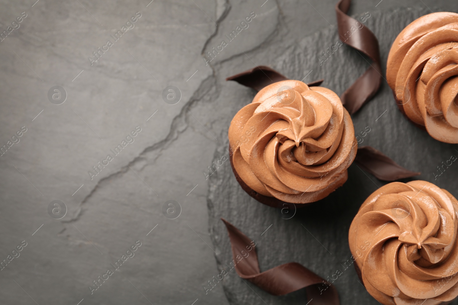 Photo of Delicious fresh chocolate cupcakes on black slate table, top view. Space for text