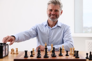 Photo of Man turning on chess clock during tournament at table indoors