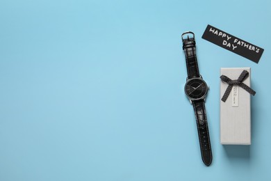 Photo of Card with phrase HAPPY FATHER'S DAY, wristwatch and gift box on light blue background, flat lay. Space for text