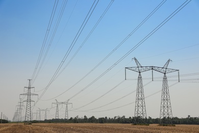 Photo of High voltage towers with electricity transmission power lines in field on sunny day