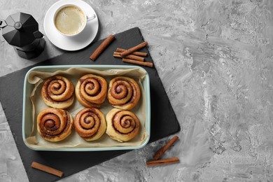 Baking dish with tasty cinnamon rolls, sticks and coffee on grey textured table, flat lay. Space for text
