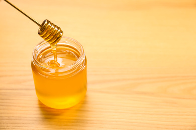 Photo of Honey dripping from dipper into jar on wooden table. Space for text