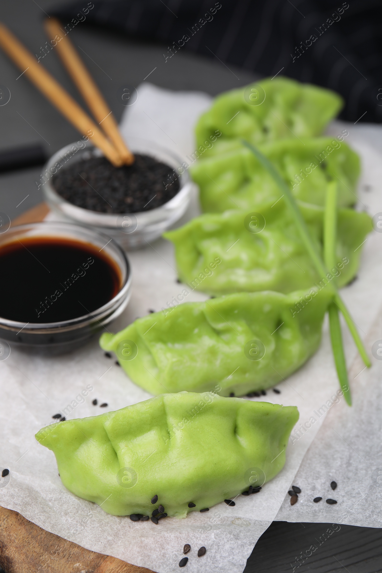 Photo of Delicious green dumplings (gyozas), soy sauce and sesame seeds on table, closeup