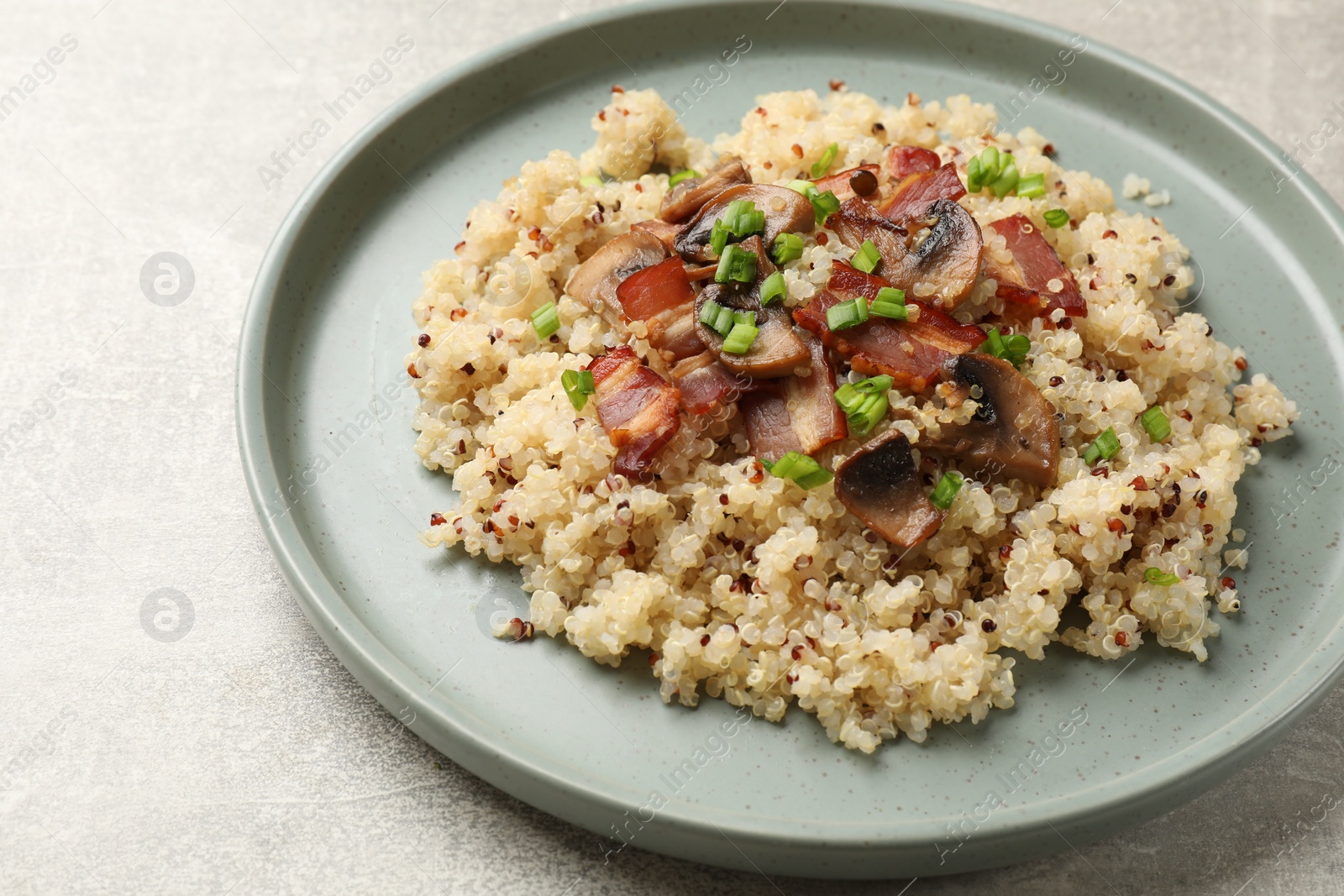 Photo of Plate of tasty quinoa porridge with fried bacon, mushrooms and green onion on light grey table, closeup