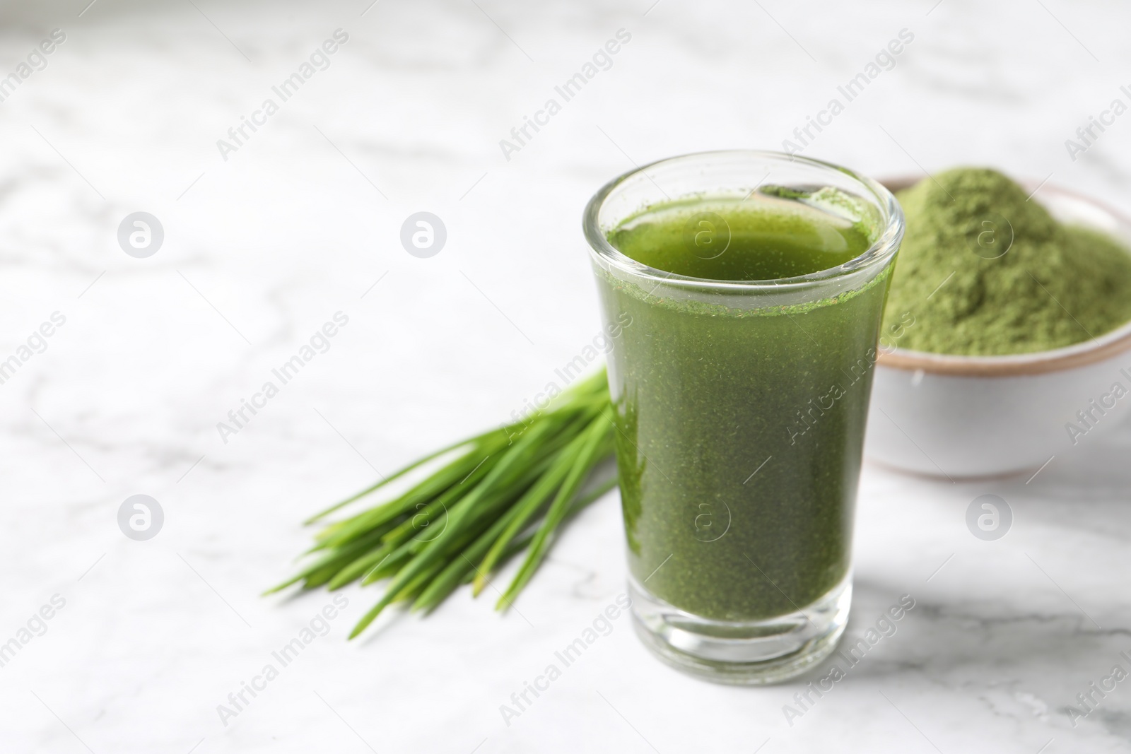 Photo of Wheat grass drink in shot glass on white marble table, closeup. Space for text