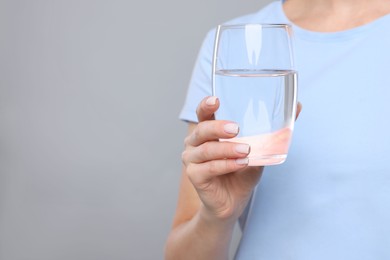 Photo of Healthy habit. Closeup of woman holding glass with fresh water on grey background, space for text