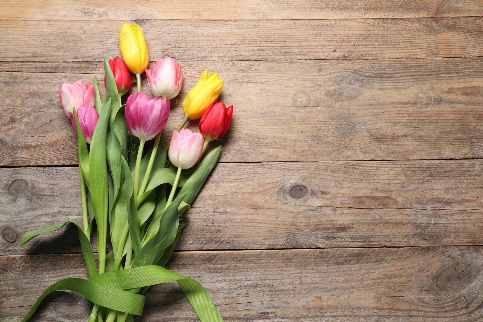 Photo of Beautiful colorful tulip flowers and ribbon on wooden table, flat lay. Space for text